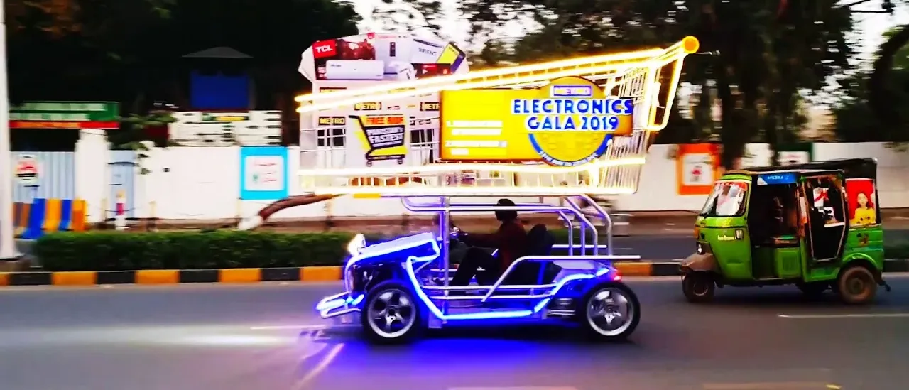 An oversized illuminated shopping-trolley float built for Metro Cash & Carry, on the road in Lahore