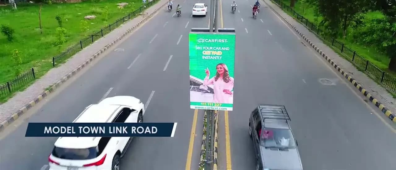 Car First creative on a central-median board along Model Town Link Road, Lahore